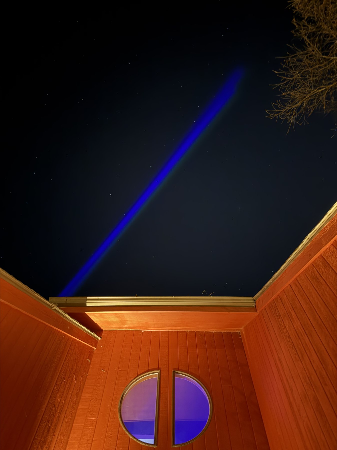 Blue synchronized lighting beam projected into the night sky above SodaPop House